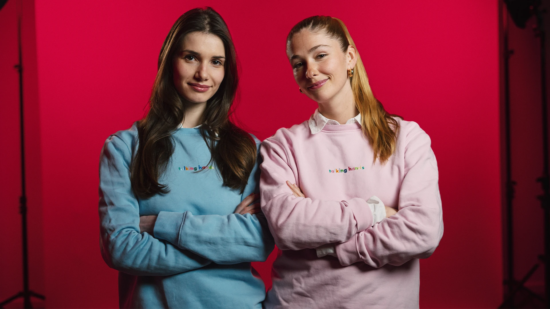 Die Gründerinnen Laura und Maria von Talking Hands stehen vor einem roten Hintergrund.