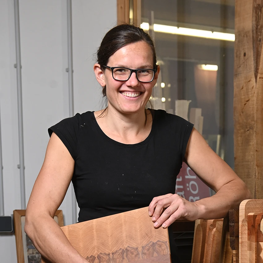 Johanna Röh hält ein Stück Holz in ihren Händen und steht in ihrer Werkstatt