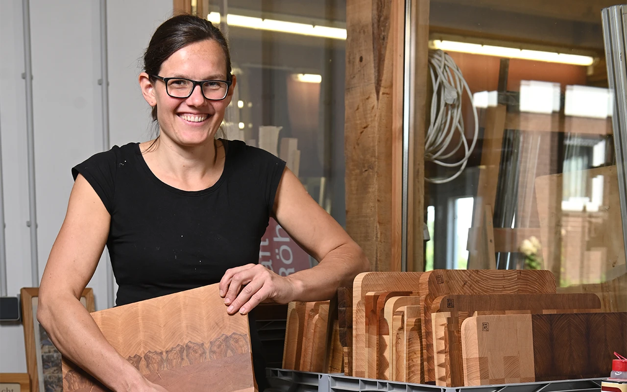 Johanna Röh hält ein Stück Holz in ihren Händen und steht in ihrer Werkstatt