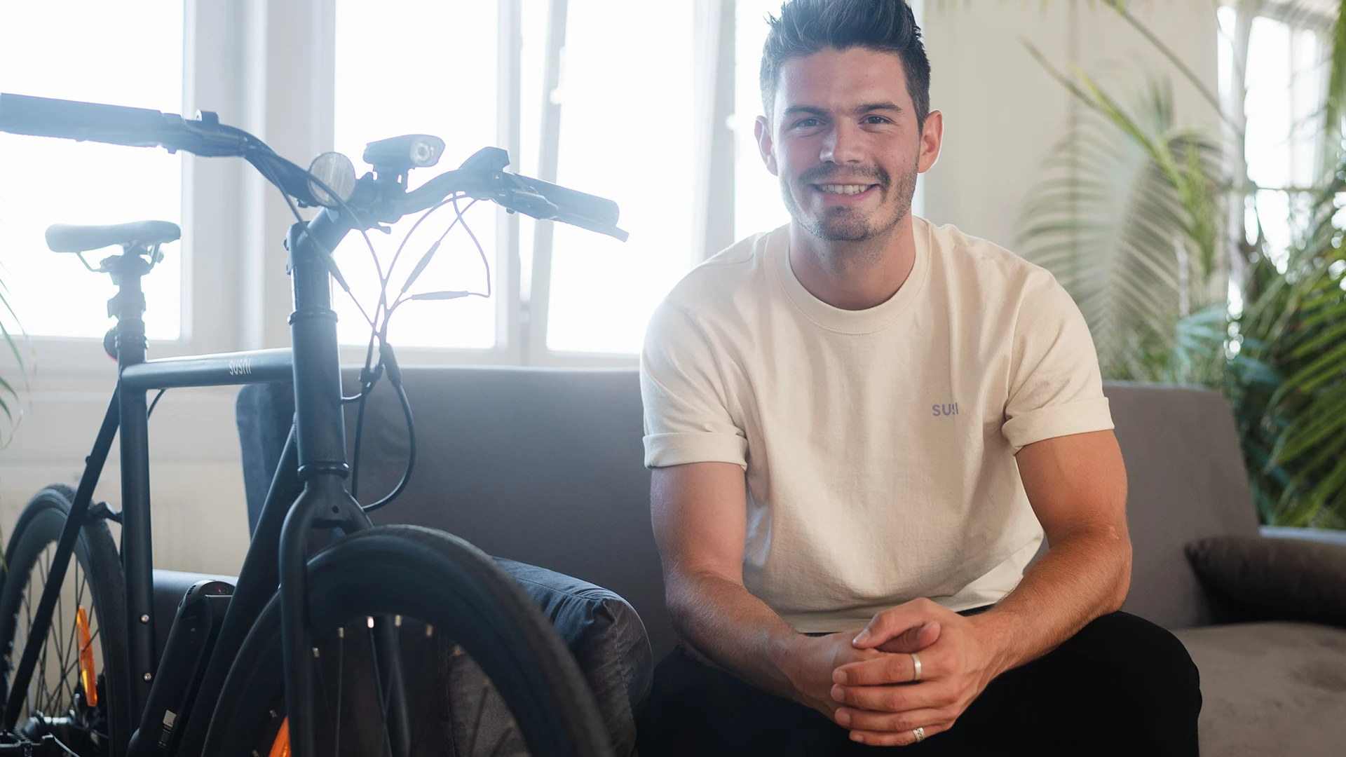 Andy Weinzierl sitzt auf einem Sofa und neben ihm steht ein E-Bike
