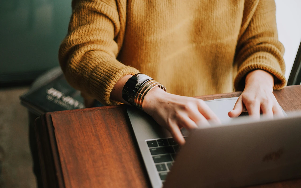 Frau sitzt am Schriebtisch und tippt auf ihren Laptop.