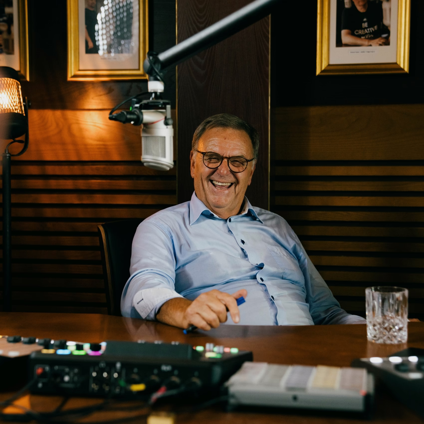 Roland Mack lacht im Podcaststudio vor einem Mikrofon.