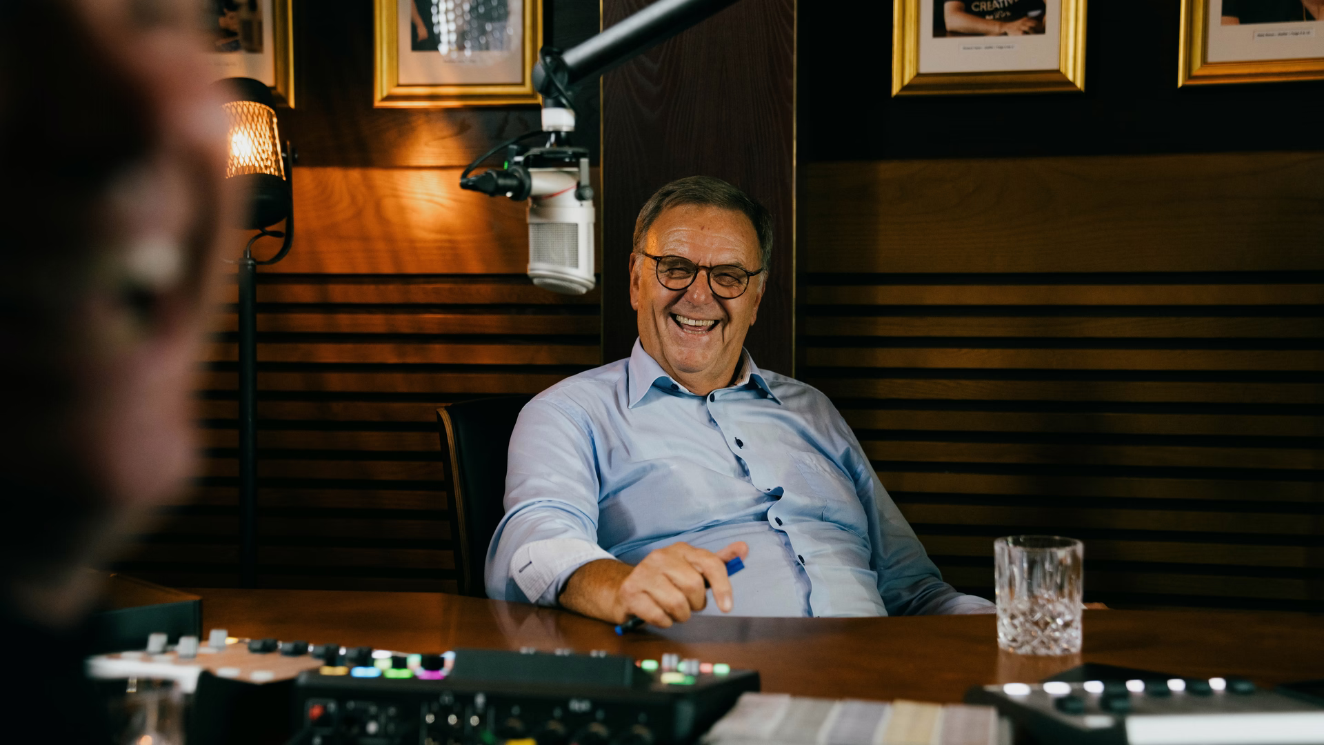 Roland Mack lacht im Podcaststudio vor einem Mikrofon.