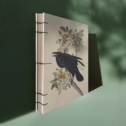 Handgebundenes Notizbuch mit sichtbarer koptischer Bindung und Raben-Motiv auf dem Deckel.