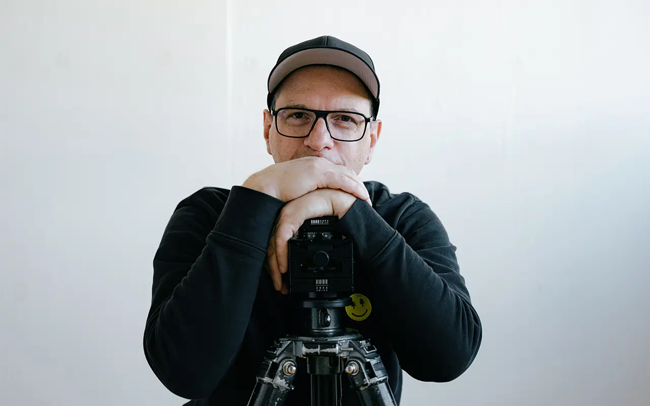 Christoph Duepper stützt die Arme auf ein Stativ und blickt in die Kamera.