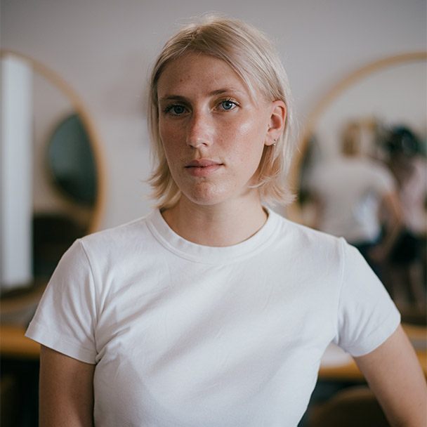 Porträt von Franka Bähr im weißen T-Shirt, im Hintergrund die runden Spiegel ihres Salons.