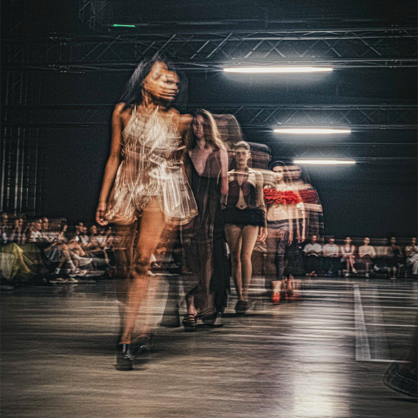 Models laufen bei einer Modenschau über den Laufsteg, aufgenommen mit Bewegungsunschärfe.