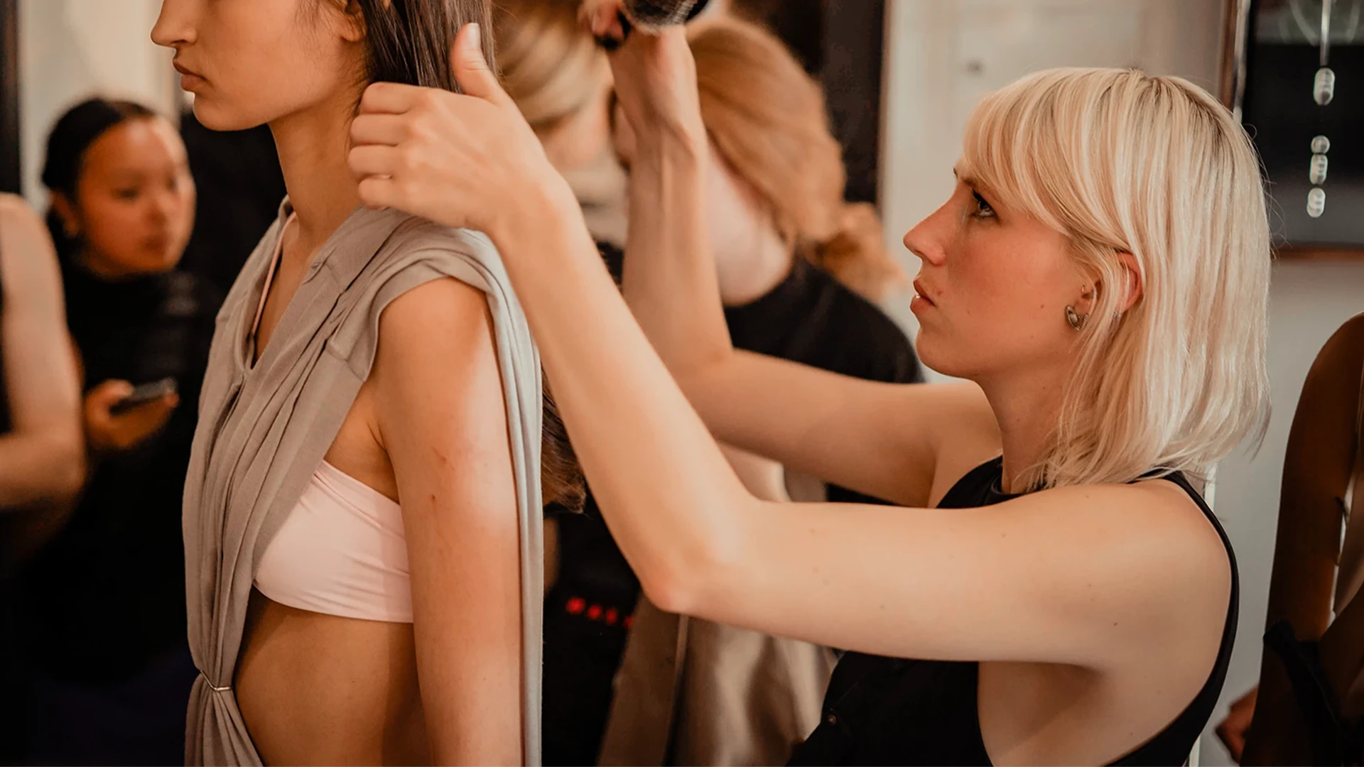 Franka Bähr bürstet backstage bei einer Modenschau die Haare eines Models, dahinter weitere Personen am Set.