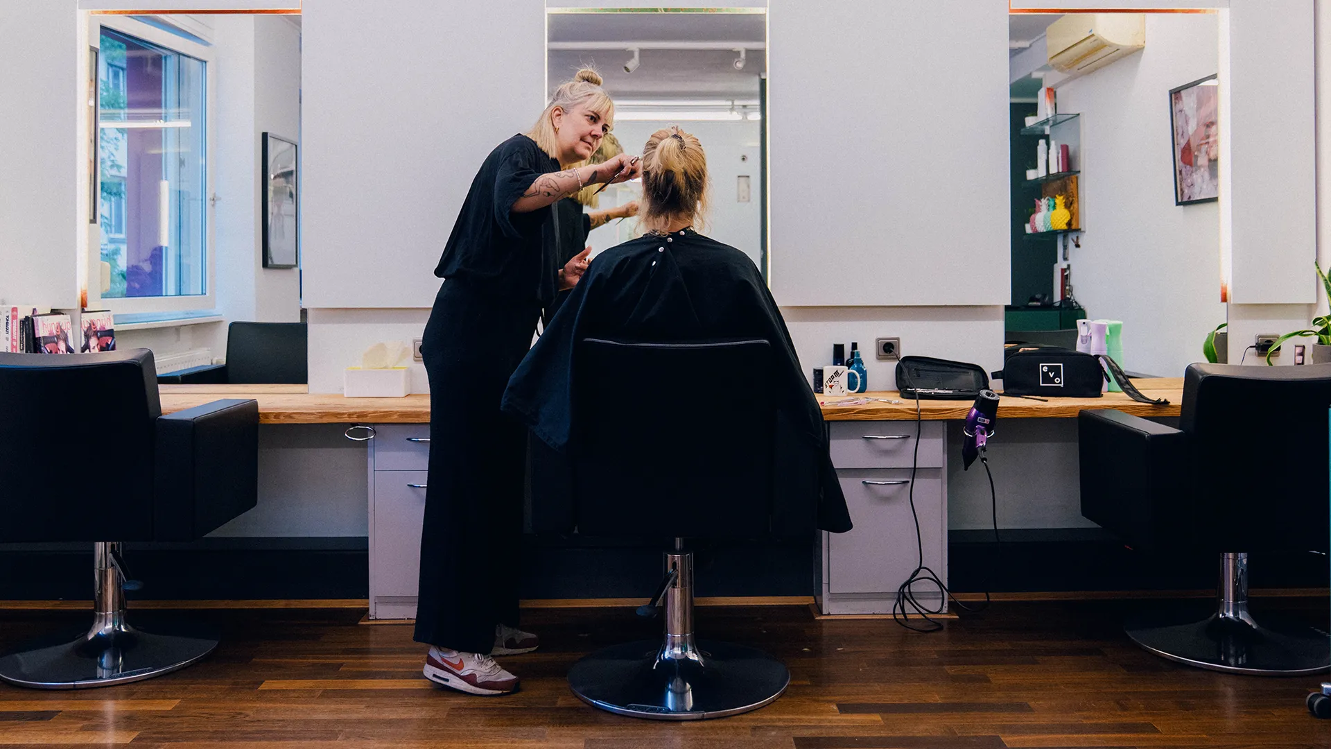 Steffi Schöne schneidet einer Kundin die Haare, im Hintergrund die Spiegelwand und der Holztresen ihres Salons.