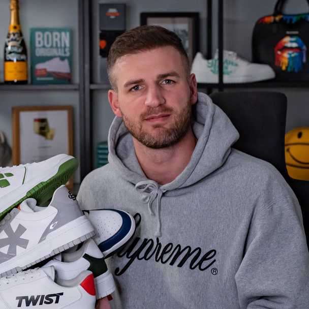 Melvin Lamberty hält einen Stapel individuell gestalteter Sneaker mit Firmenlogos im Arm.