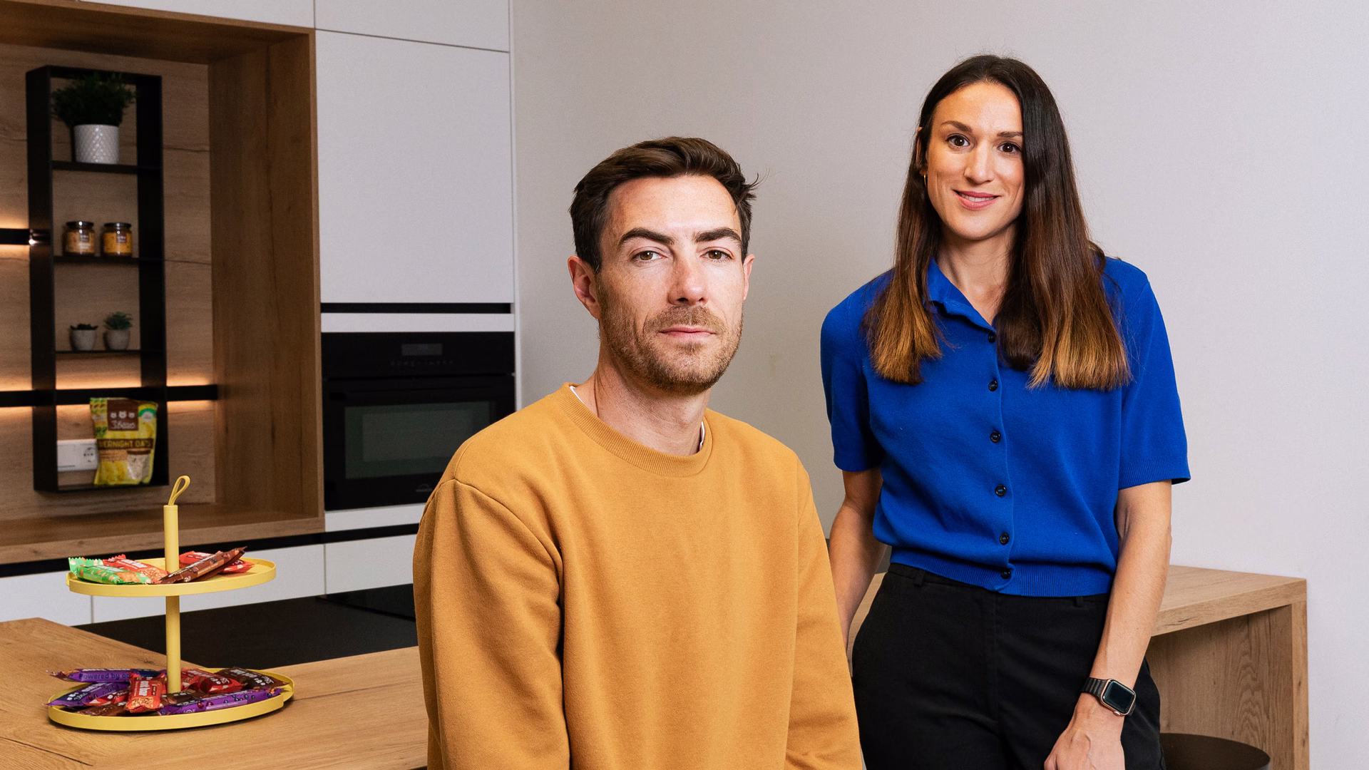 Caroline und Tim Nichols stehen nebeneinander in einer hellen Küche, auf der Theke vor ihnen eine Etagere mit 3Bears-Riegeln.