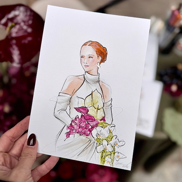 Eine Hand hält eine Modeillustration: rothaarige Frau in weißem Neckholder-Kleid mit pinkem Blumenstrauß.