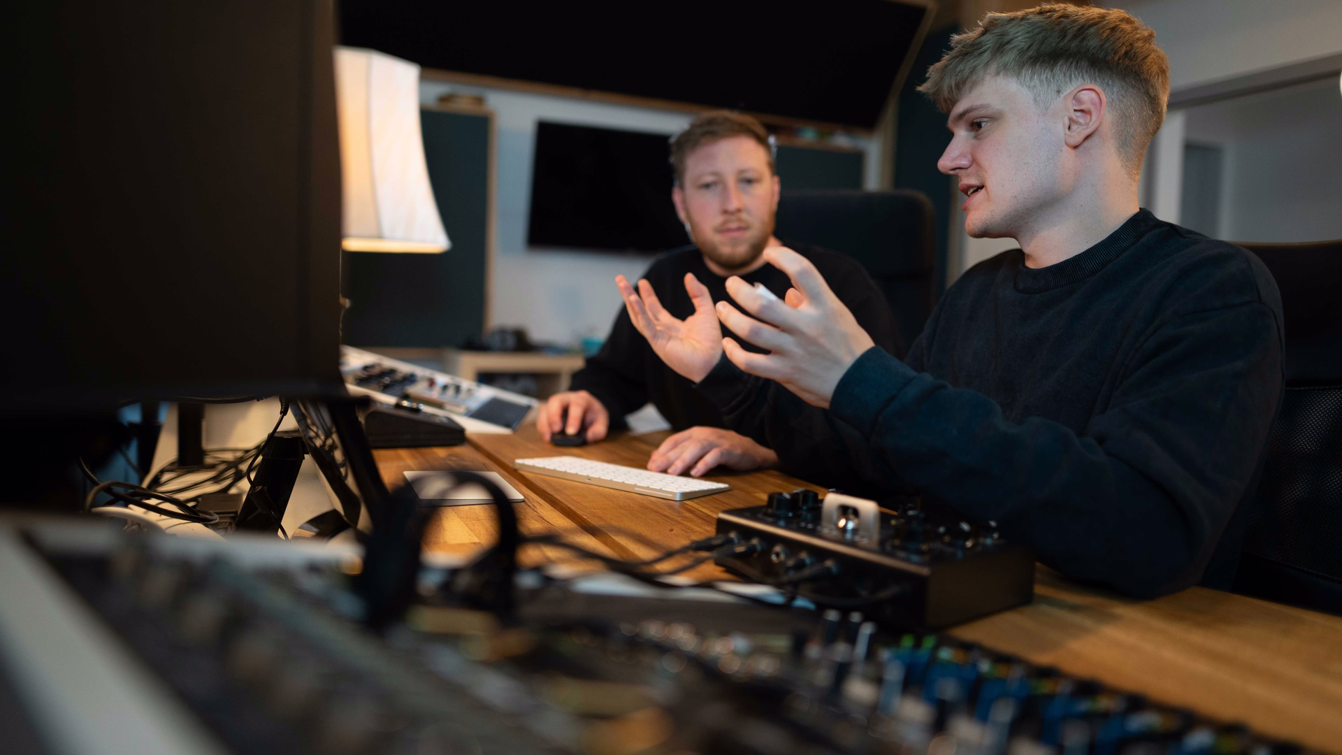 Martin Meyer erklärt im Tonstudio gestikulierend etwas, neben ihm hört ein Kollege zu, vorn unscharf Mischpult und Technik.