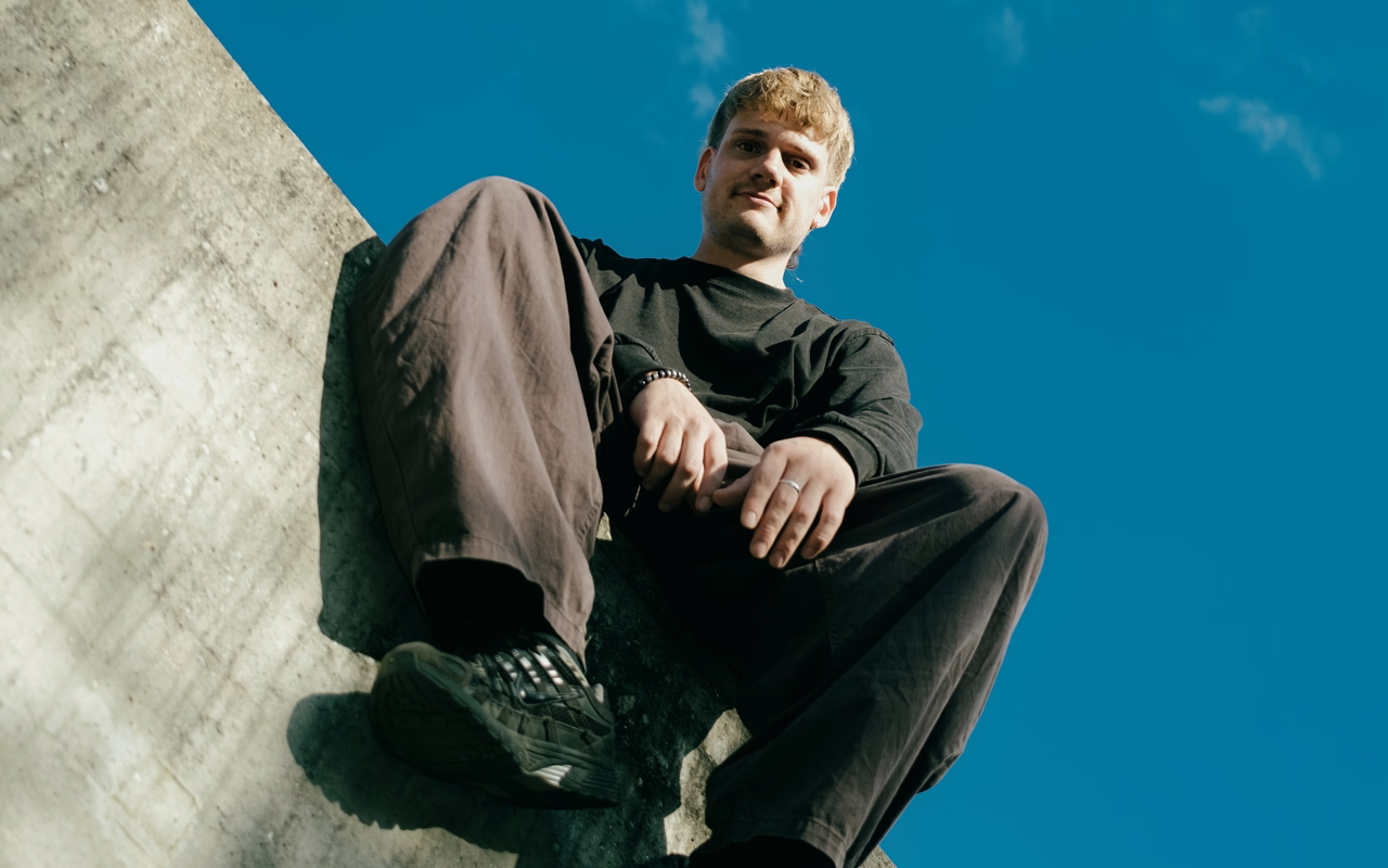Martin Meyer sitzt auf einer Betonmauer und blickt von oben in die Kamera, hinter ihm blauer Himmel.