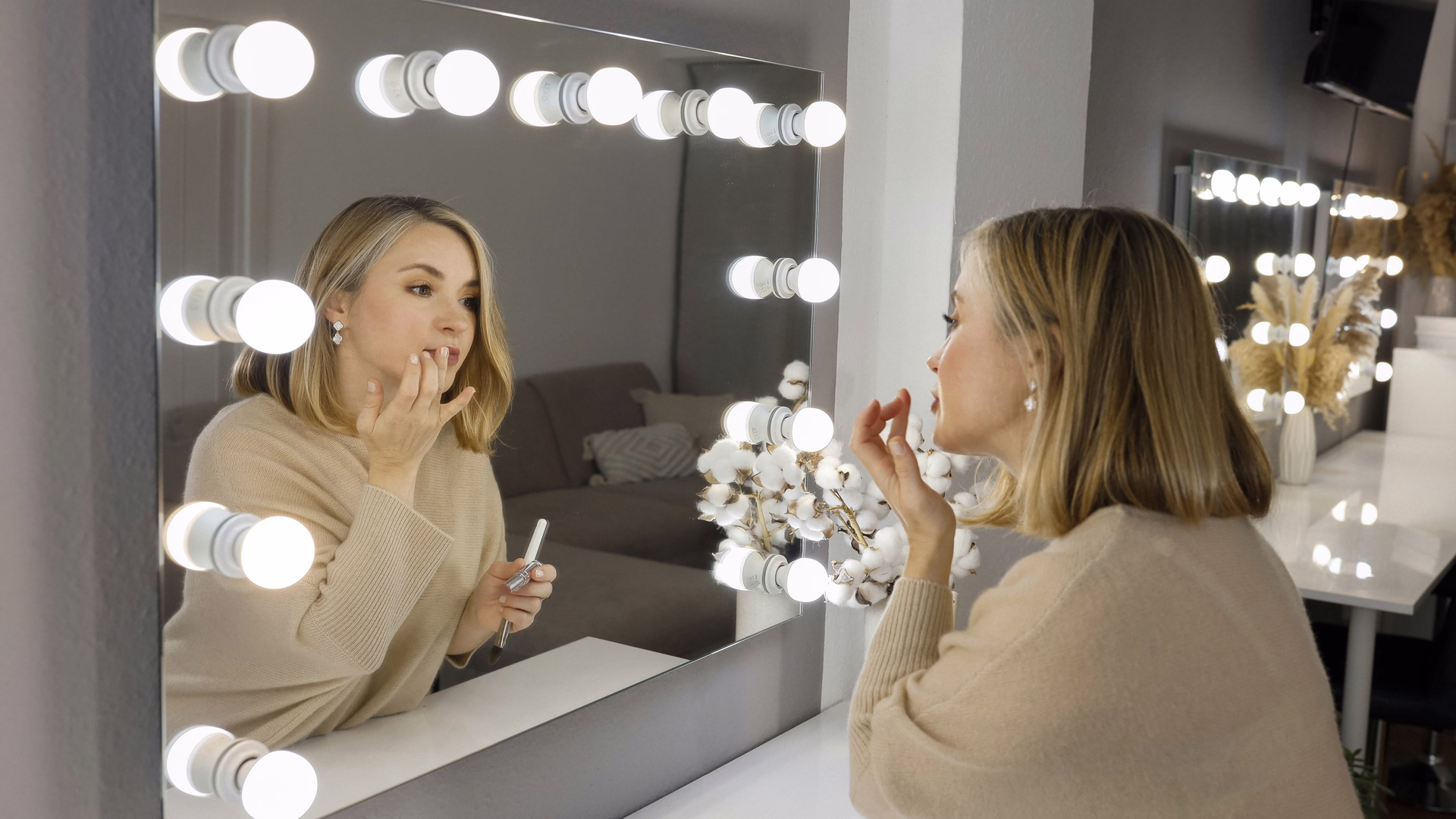 Elena Bärweg trägt vor einem beleuchteten Schminkspiegel Lippenfarbe auf, ihr Spiegelbild blickt zurück.