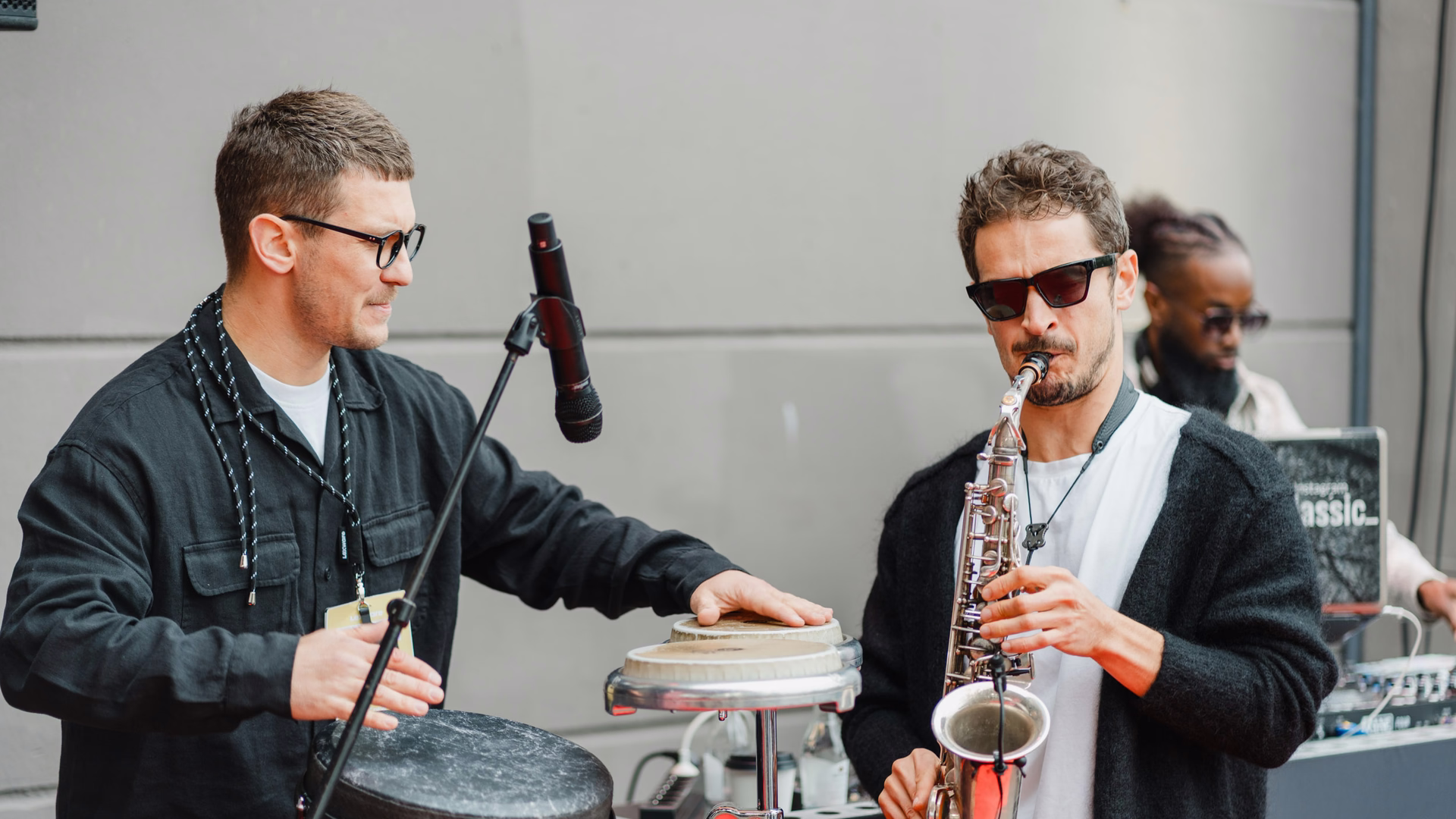 Kamil Khusyainov spielt mit Sonnenbrille Saxophon, neben ihm trommelt ein Musiker auf einer Handtrommel, im Hintergrund legt ein DJ auf.