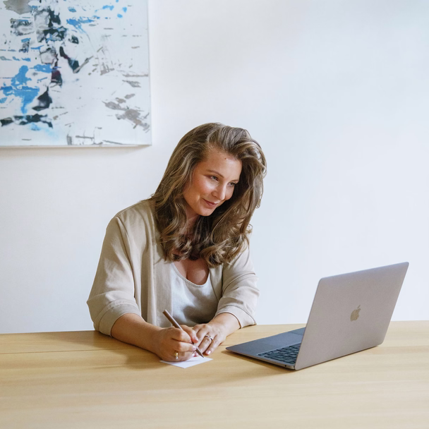 Sarah-Lisa Besemer sitzt an einem Holztisch, macht sich Notizen und schaut auf ihren Laptop.