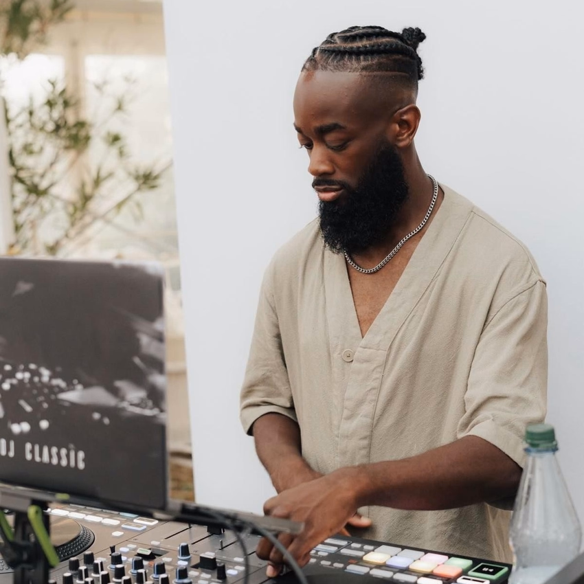 Noel Tagoe mischt mit beiden Händen am DJ-Pult, links ein Laptop mit der Aufschrift „DJ Classic“.