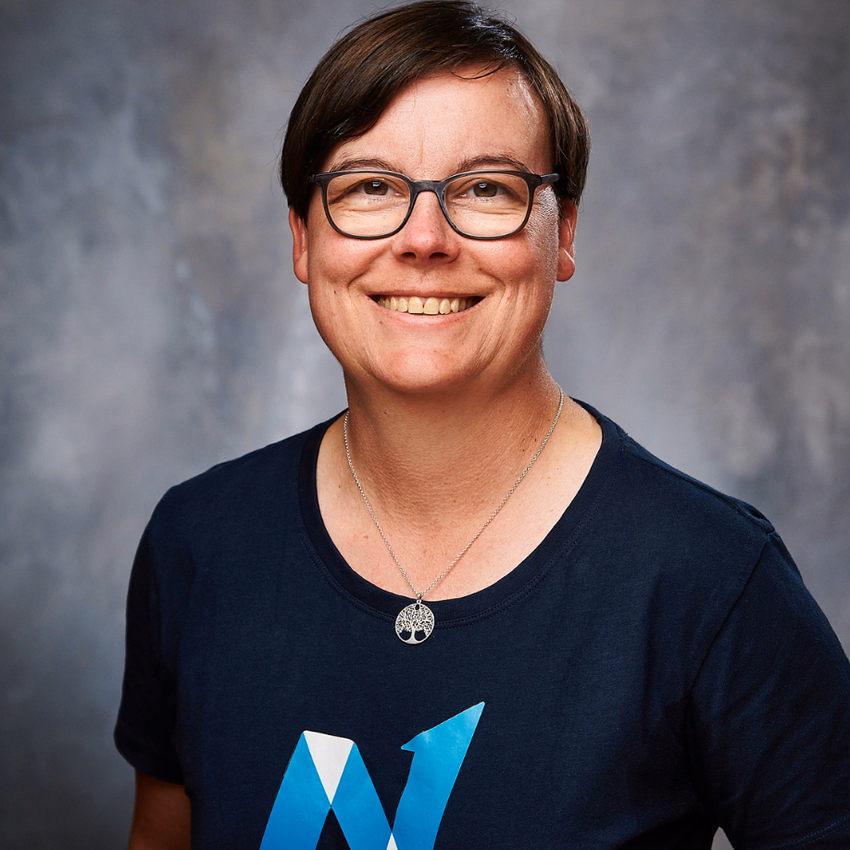 Britta Behrens lächelt in die Kamera, Studioporträt vor grauem Hintergrund.