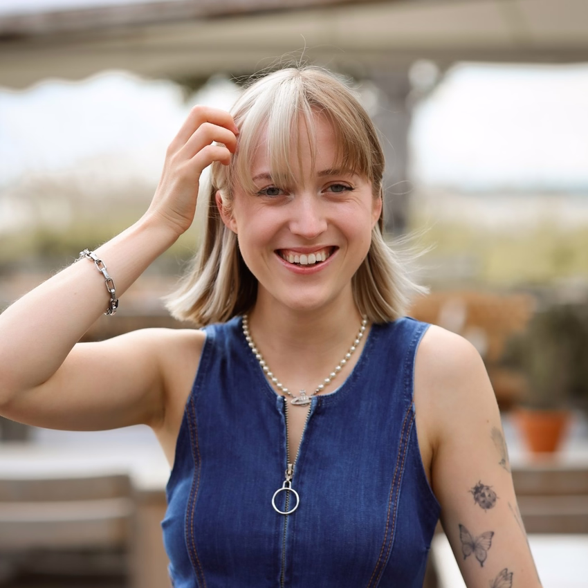 Nele Burgstaler lacht und streicht sich die Haare aus dem Gesicht, im Hintergrund eine sonnige Dachterrasse.