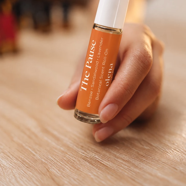 Eine Hand hält einen orangefarbenen Roll-on mit der Aufschrift The Pause über einem Holztisch.