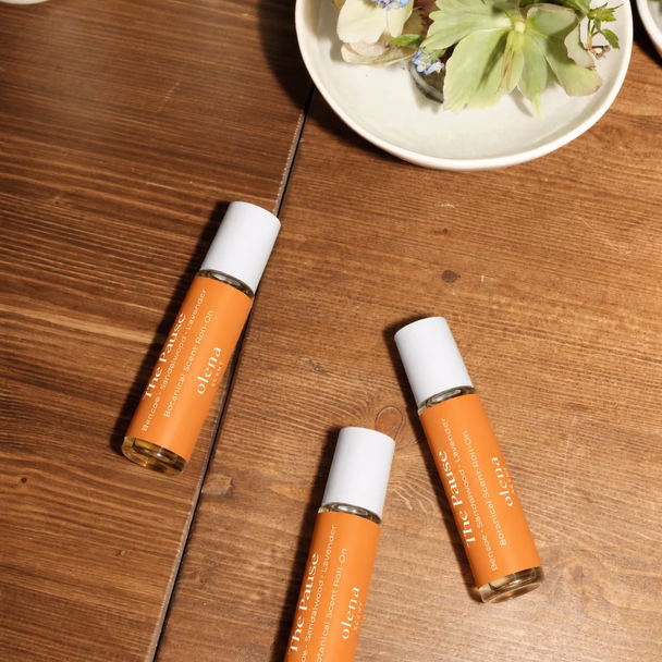 Drei orangefarbene Roll-ons liegen auf einem Holztisch neben einer Schale mit Blumen.