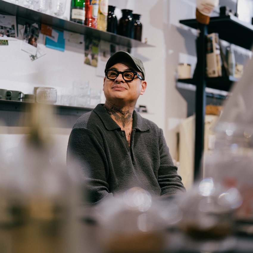 Karl Sütterlin mit Kappe, Brille und dunklem Strickpullover blickt zufrieden über die Theke seines Ladens in Freiburg.