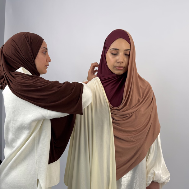 Zwei Frauen vor weißem Studiohintergrund, eine legt der anderen einen Jersey-Hijab über die Schulter.