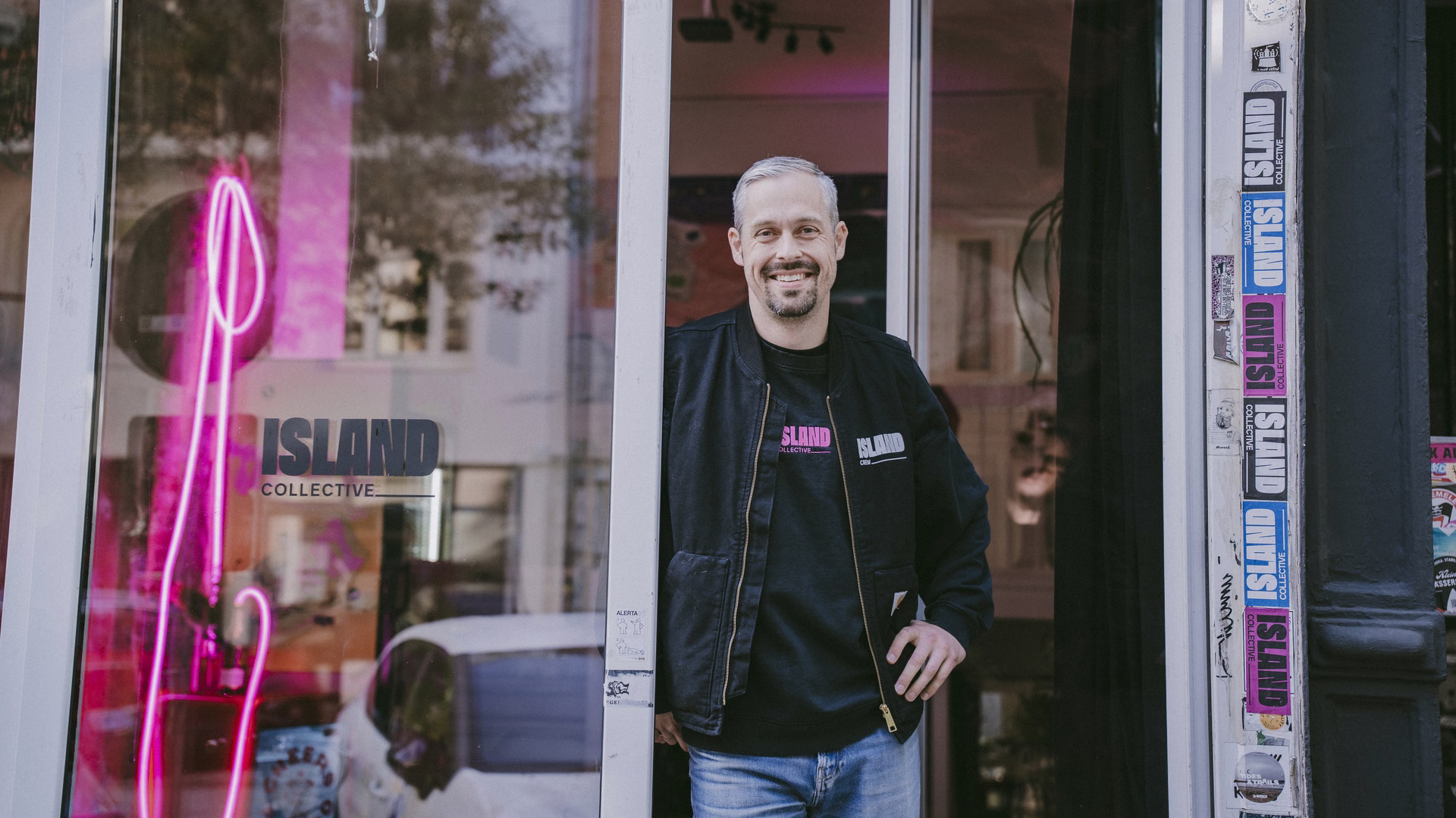 Florian Laudon steht lächelnd in der offenen Tür des Island-Collective-Ladens, im Schaufenster leuchtet pinkes Neonlicht.