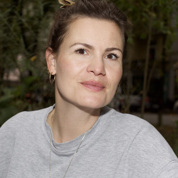 Melanie Wildt vor grünen Sträuchern, den Blick in die Kamera gerichtet.
