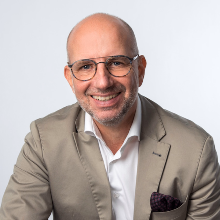 Frank Bergemann im beigen Sakko lächelt vor hellem Hintergrund.