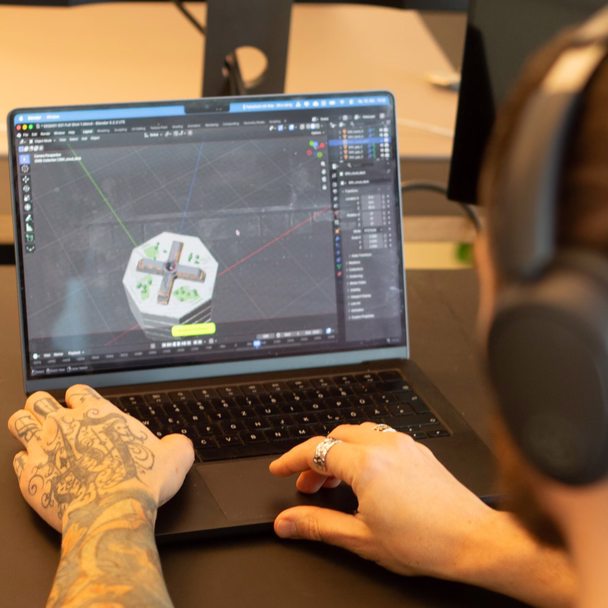 Blick über die Schulter auf einen Laptop, auf dem ein 3D-Modell in Blender bearbeitet wird.