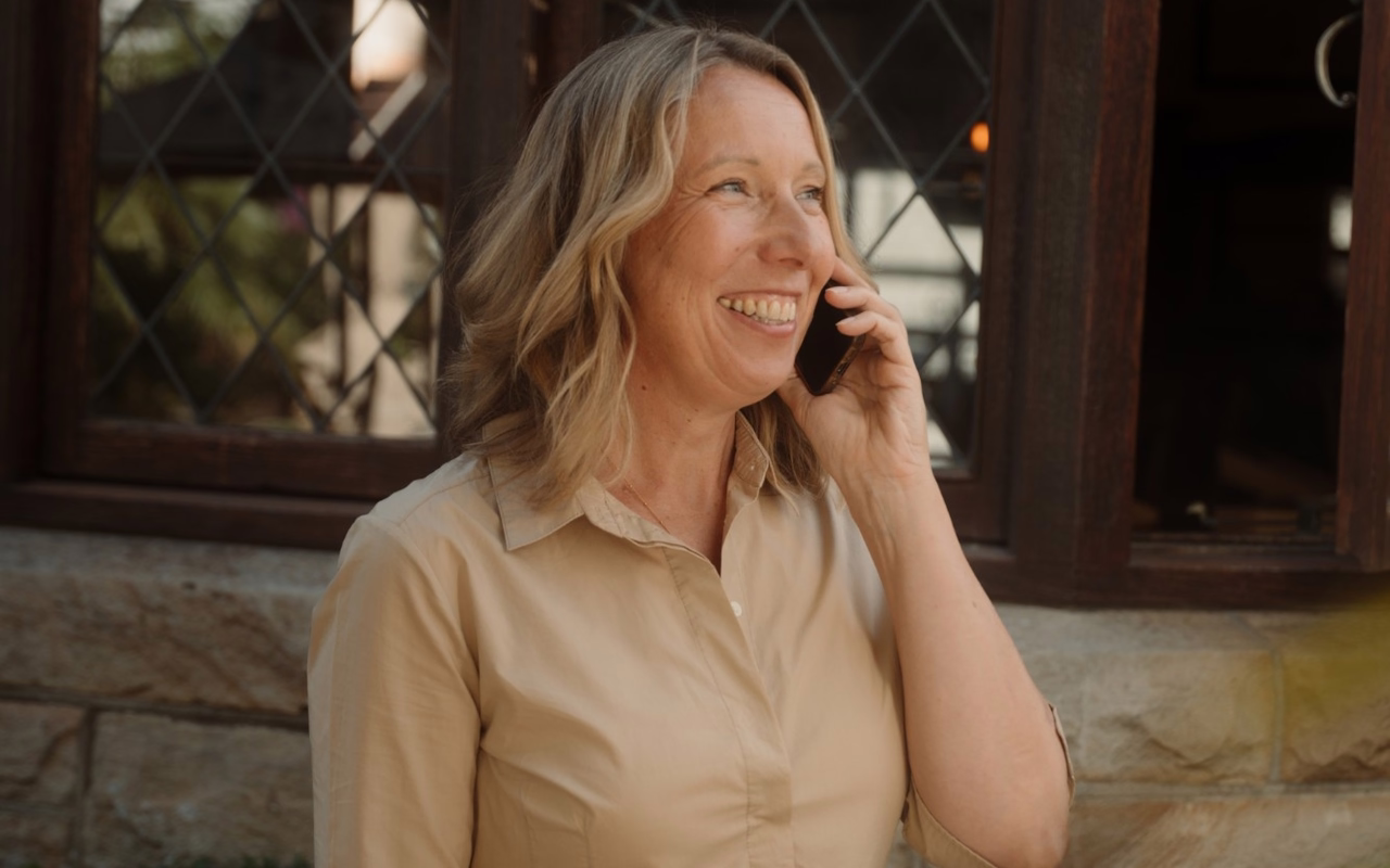 Anja Helming telefoniert vor einem Gebäude und hält einen Laptop unter dem Arm.