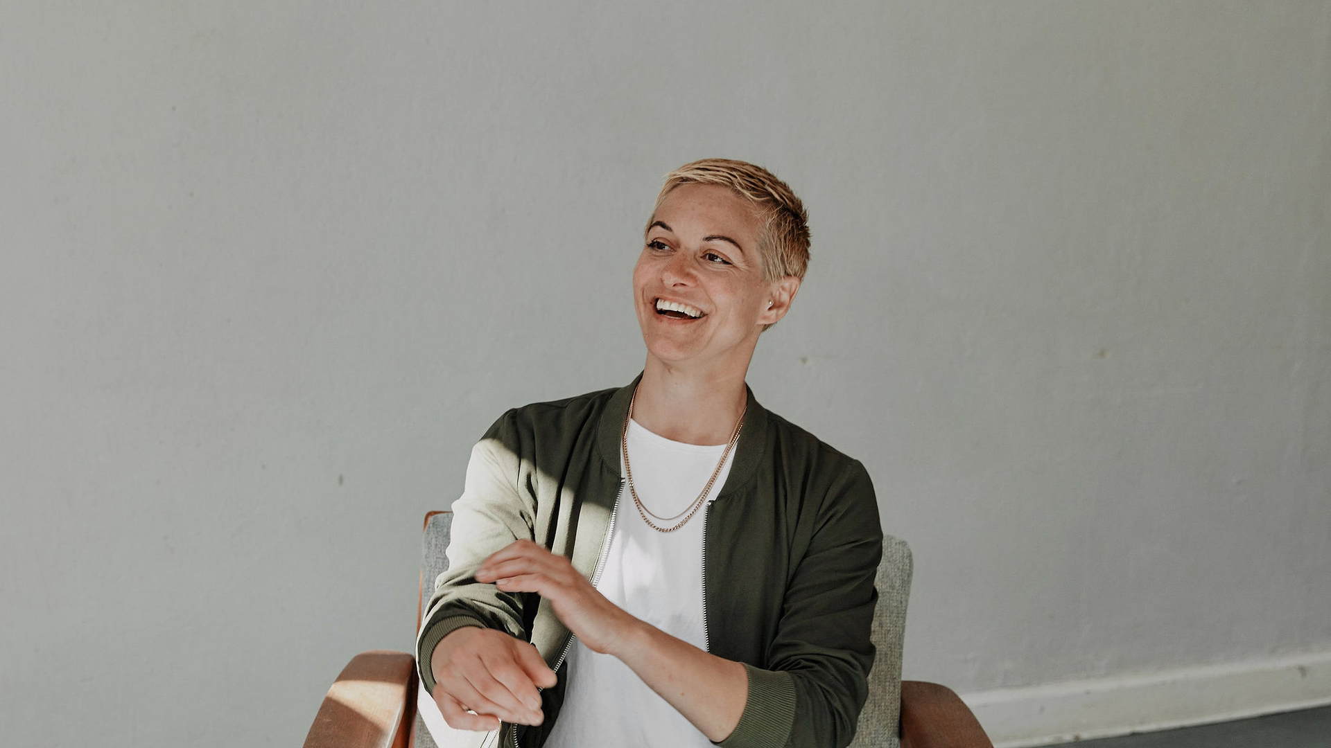 Stefanie Treiber sitzt vor einer hellen Wand und lacht zur Seite.