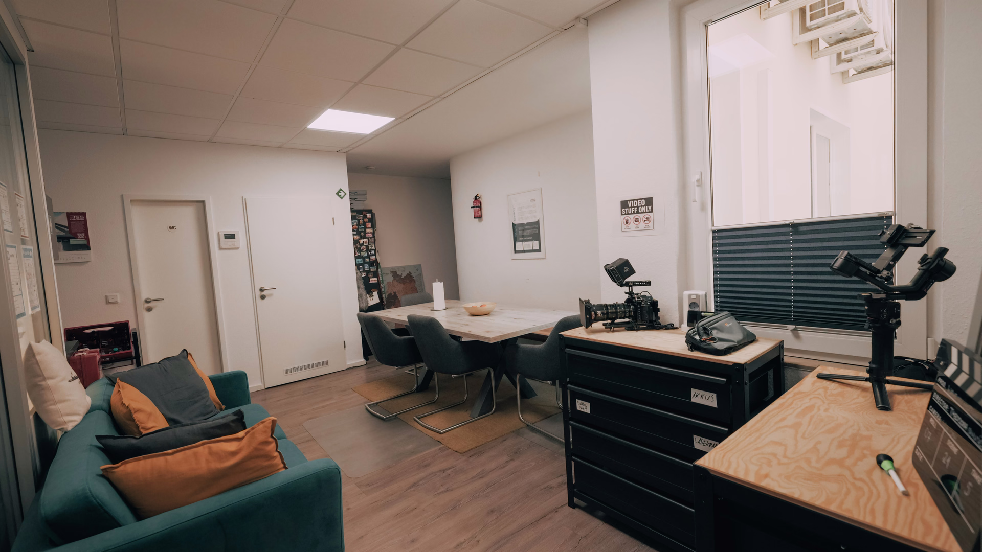 Büro von Wave In Motion mit petrolfarbenem Sofa, Besprechungstisch und einer Filmkamera samt Gimbal auf einer Kommode.