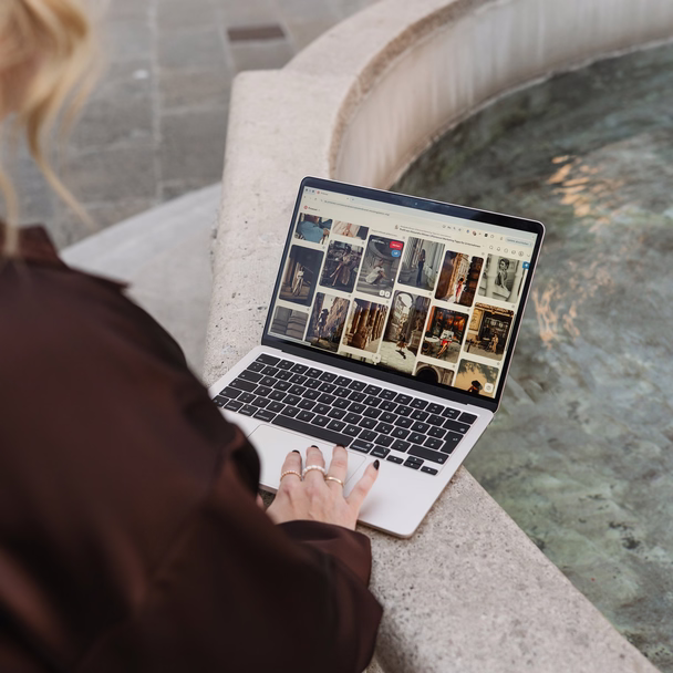 Hand auf dem Trackpad eines Laptops auf einem Brunnenrand, auf dem Bildschirm ein Pinterest-Profil.