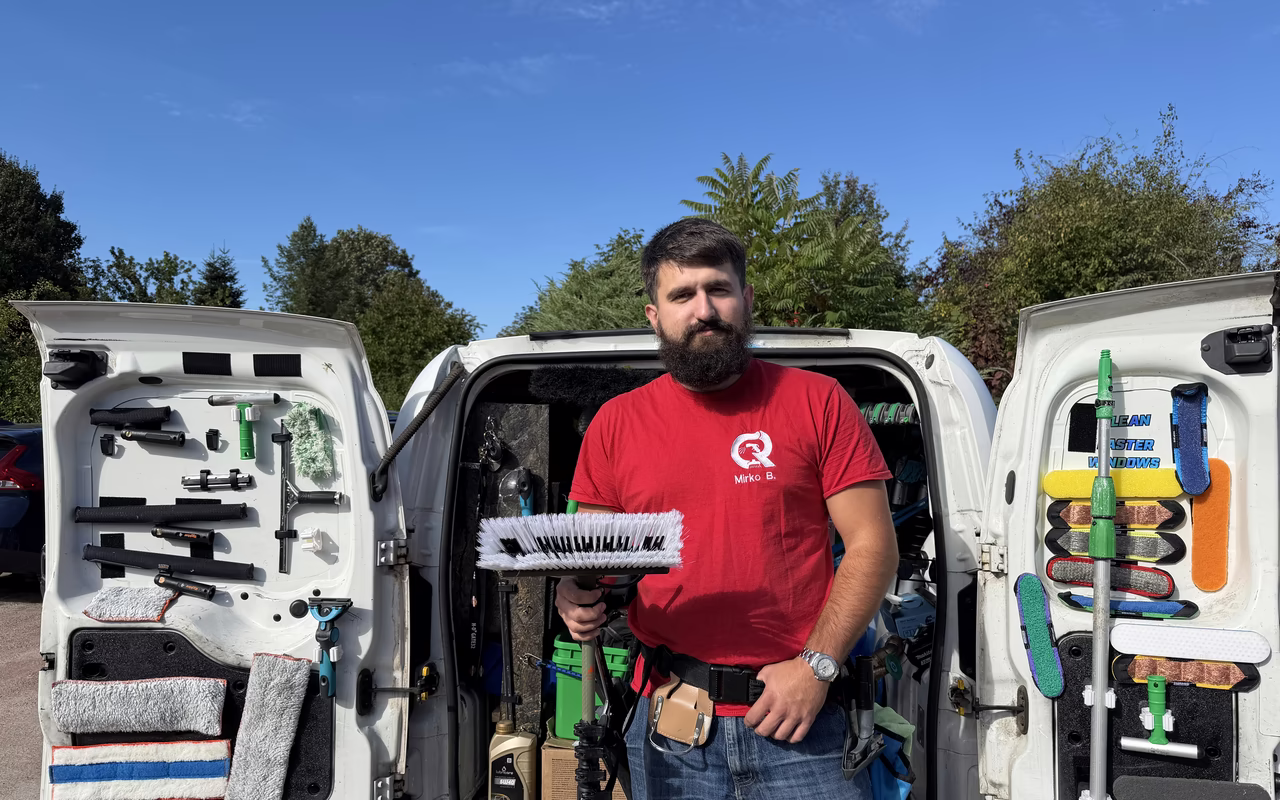 Mirko Bilić im roten Firmenshirt zwischen den offenen Hecktüren seines Transporters, darin Bürsten, Abzieher und Reinigungsmittel.