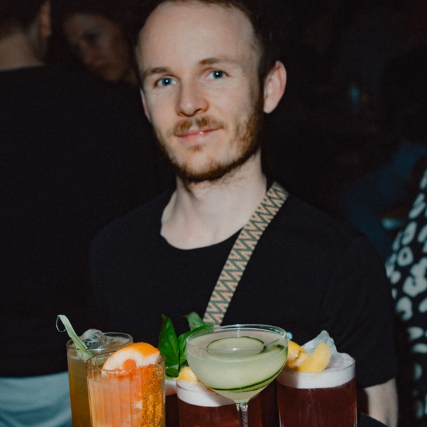Ein Bartender trägt im Gastraum des FREDERICS ein Tablett mit vier Cocktails.