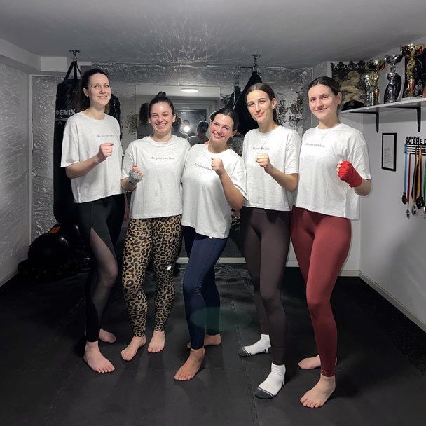 Fünf Frauen stehen nach einem Training in der Kampfsportschule nebeneinander und heben die Fäuste.