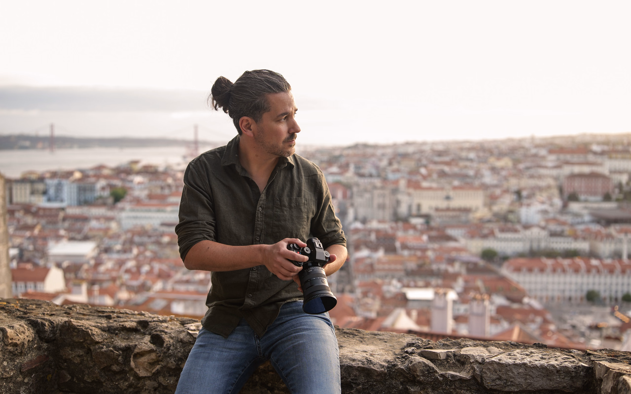 Andreas Abb sitzt mit seiner Kamera auf einer Mauer über den Dächern von Lissabon.