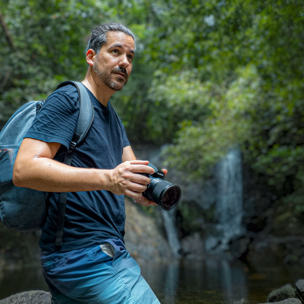 Andreas Abb kniet mit seiner Kamera an einem Wasserfall im Dschungel.