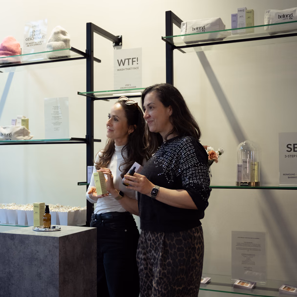 Julia Kiener und ihre Mitgründerin Joa Bürger betrachten Produkte an einem Verkaufsregal von belong. cosmetics.