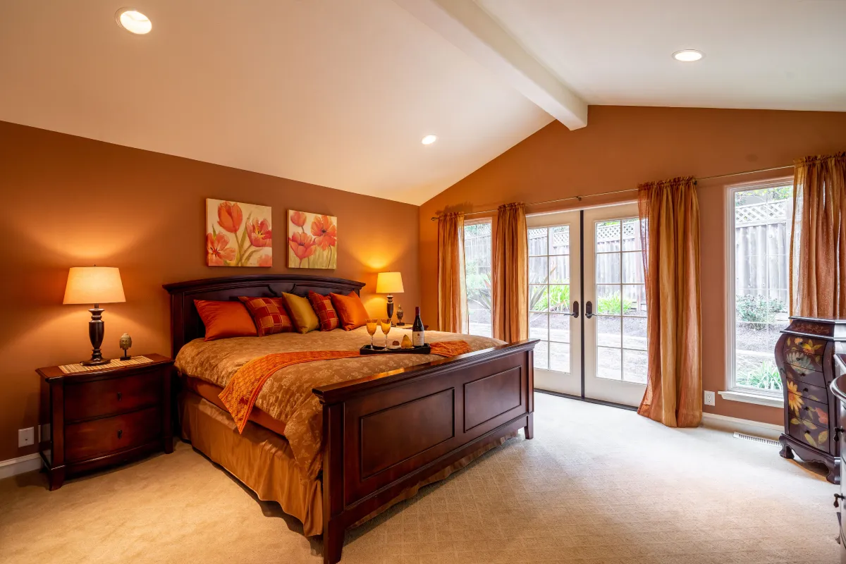 A wide view of the master bedroom with a King bed, full of warm ochre and brown tones.