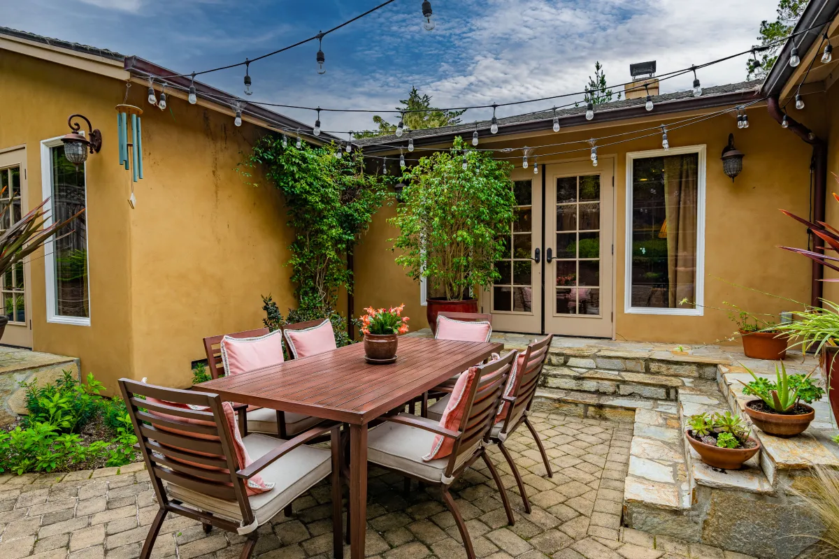 The backyard dining area with greenery, bay lights, and tiled/stoned steps and ground.