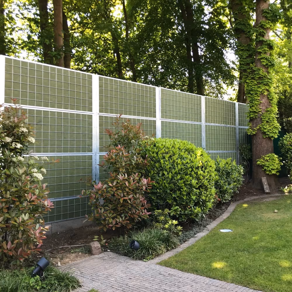 garden with a noistop galvanized steel fence in it, with green bushes in front and trees in the background.