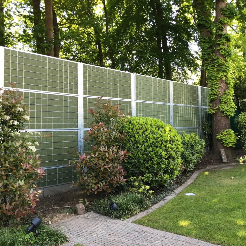 garden with a noistop galvanized steel fence in it, with green bushes in front and trees in the background.
