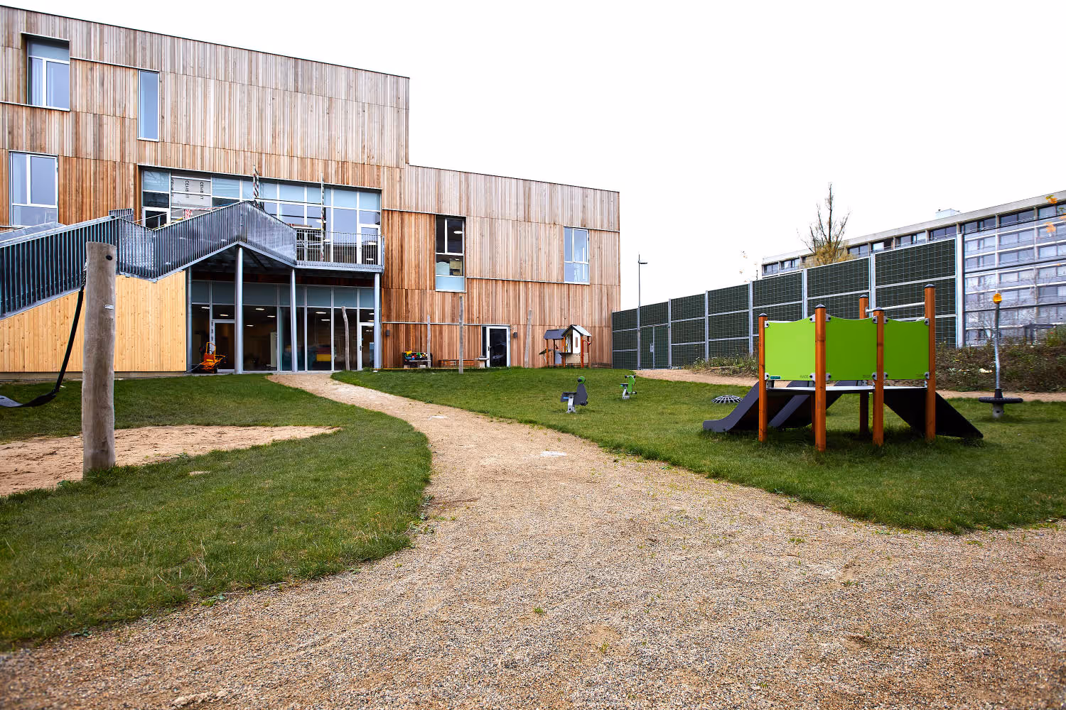 Une école avec un design en lattes de bois et une clôture antibruit autour du périmètre.