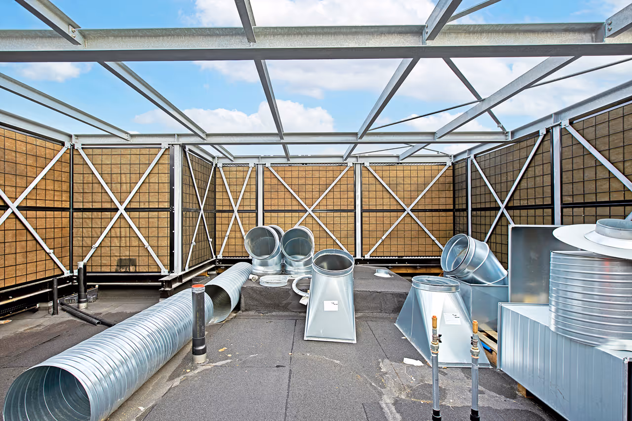 Rooftop with steel framework and brown acoustic fencing enclosing HVAC ductwork and vents.