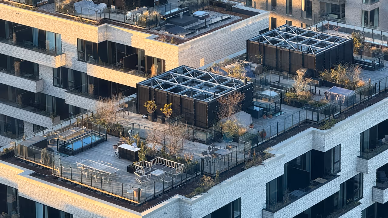 Rooftop terrace with outdoor furniture, plants, pergolas, and glass railings on a modern building.