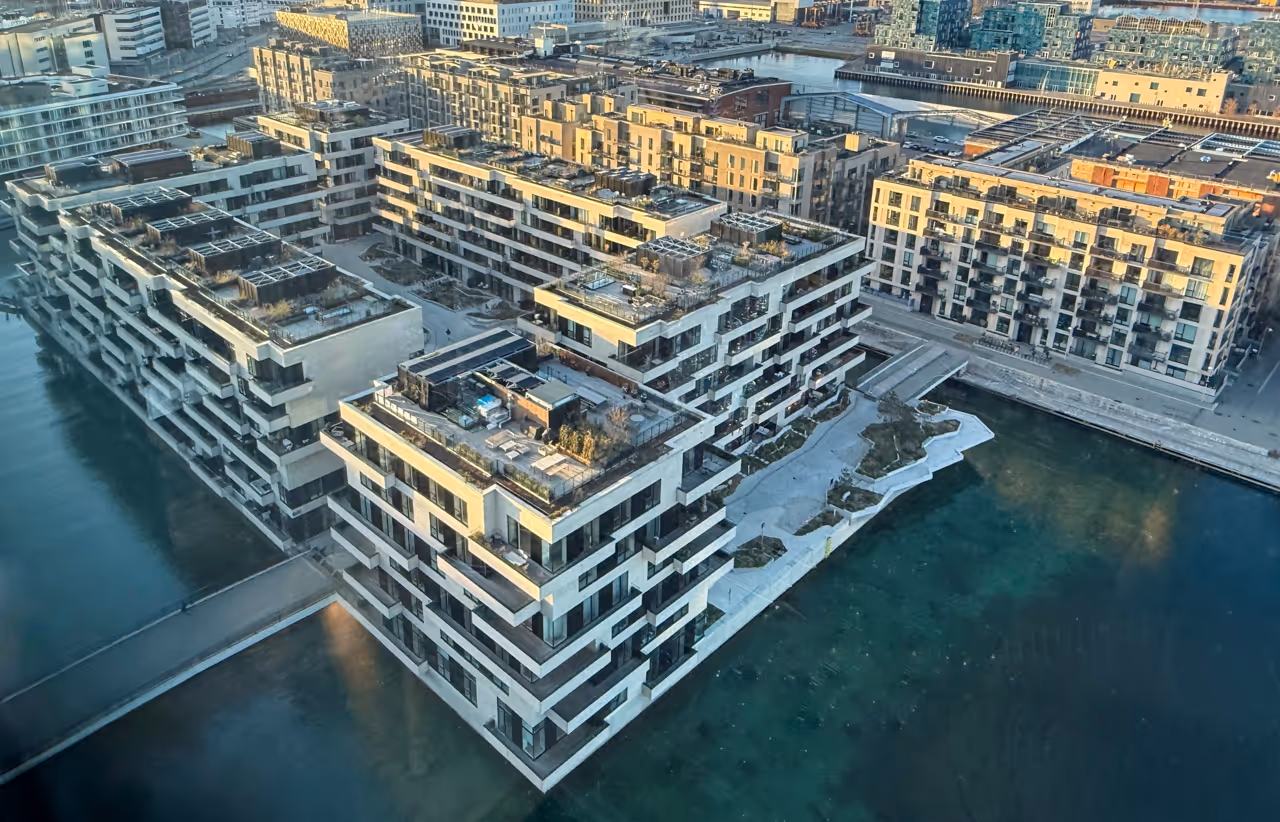 Aerial view of modern waterfront apartment complex with terraces and balconies over clear water.